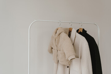 Wall Mural - Warm autumn seasonal baby and adult clothes on hanger over white wall. Woolen neutral beige, white and black jackets. Minimalist fashion clothes wardrobe