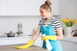 © Pixel-Shot - Happy young woman in yellow rubber gloves cleaning dining table with rag and detergent