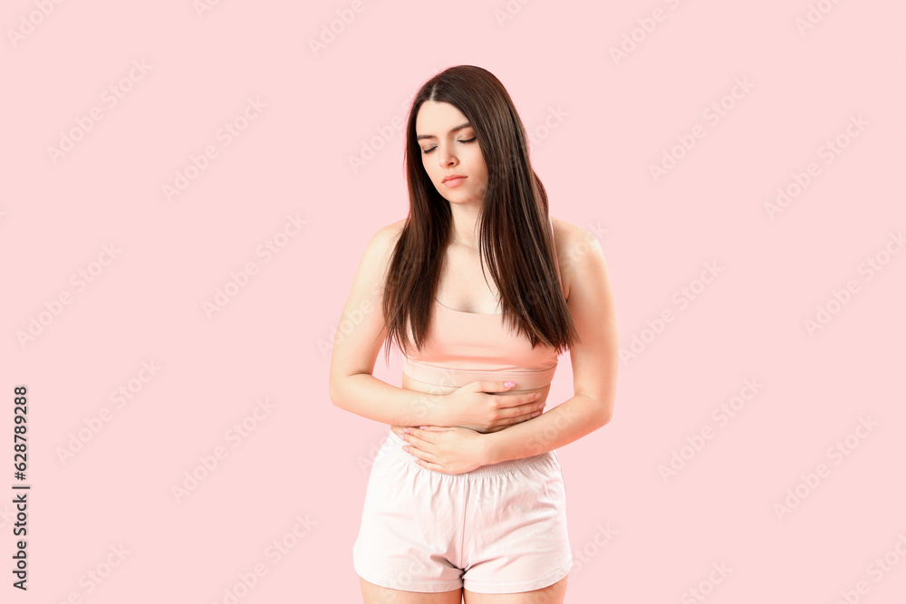 Young woman having menstrual cramps on pink background