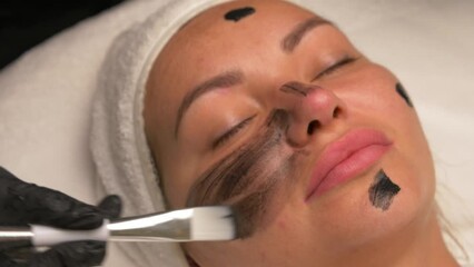 Canvas Print - cosmetologist applying black mask on pretty woman face wearing black gloves, gorgeous woman in spa having facial procedures