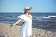 © rogerphoto - Happy blonde woman is on the ocean beach in a white dress and sunglasses, open arms