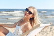 © rogerphoto - Happy blonde woman wearing sun glasses and relaxing on a wooden deck chair at the ocean beach