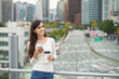 © Dialogue Frame - A young woman is resting on a land bridge with coffee and a smartphone in the background of a busy street during the day.