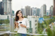 © Dialogue Frame - A young woman is resting on a land bridge with coffee and a smartphone in the background of a busy street during the day.