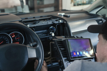 Auto electrician or repairman in car service installs multimedia sound system or car radio in auto dashboard panel.