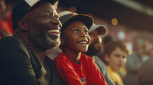 African American Grandfather And Grandson At Baseball Game. Smiling And Laughing. Enjoying The Match. Together In The Stands. Concept Of Game, Sports, Spectating, And Bonding.