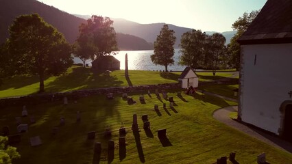 Sticker - Drone footage over an old church next to cemetery graves by the sea and alps in Norway at sunset