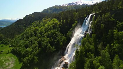 Wall Mural - Drone footage around Tvindefossen waterfall with a green forested landscape on a sunny day