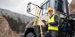 Engineer with tablet computer stands on the stairs to the cab of a truck