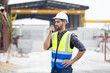 © NVB Stocker - radio transmitter. Hispanic latin architect construction Engineering man in hardhat talking on walkie talkie at factory facilities. Heavy Industry Manufacturing Factory. Prefabricated concrete walls