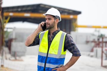 Wall Mural - building and construction worker using mobile phone, Hiapanic latin male wearing safety hard hat helmet standing with arms crossed at construction site and looking at camera