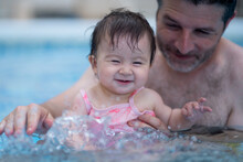 Lifestyle Portrait Of Father And Little Daughter Enjoying Summer - Man Holding Her Sweet Baby Girl Excited And Cheerful Playing Together At Resort Swimming Pool In Parenting Concept