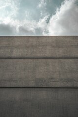 Poster - View of a street corner featuring a grey concrete wall and a bright blue sky with fluffy clouds.