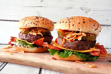 Tasty hamburgers with cheese, bacon and crispy onions. Side view table scene against a white wood background.