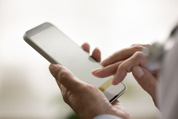 Wall Mural - Close up of blank smartphone screen in mature doctors hands. Medical practitioner woman using professional app on smartphone, touching screen, typing, holding gadget. Cropped shot