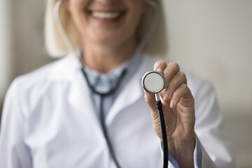 Wall Mural - Hand of positive doctor woman showing stethoscope close up. Cheerful therapist, practitioner woman promoting medical service, health checkup, smiling, holding cardiologist tool. Cropper portrait