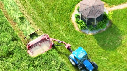 Wall Mural - Tilted downward aerial video of tractor mowing down tall grass