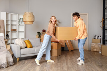 Young couple carrying cardboard box in room on moving day