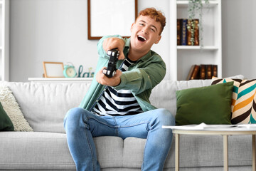 Wall Mural - Young redhead man playing video game at home