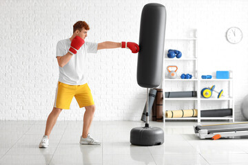 Sticker - Young redhead boxer punching bag in gym