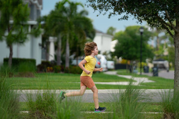 Canvas Print - Young kid running and smiling in the park. Active little kid running along street during leisure sport activity. Sporty kid running in nature. Child run. Kids running. Summer sport. Happy childhood.