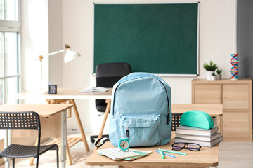 Wall Mural - Blue school backpack with stationery, eyeglasses and alarm clock on desk in classroom