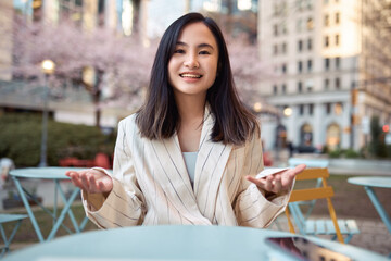 Wall Mural - Young happy Asian business woman talking to camera outdoors having hybrid work meeting, online class, giving presentation or webinar, speaking during virtual event or shooting blog. Web cam view