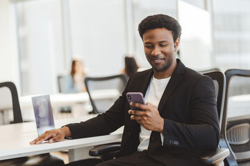 Successful African American man holding mobile phone, sitting in the modern office