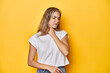 © Asier - Young blonde Caucasian woman in a white t-shirt on a yellow studio background, suffers pain in throat due a virus or infection.
