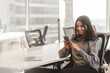 © Maria Vitkovska - Smiling Indian woman with beautiful hair wearing casual clothes holding mobile phone checking mail in modern office. Attractive female working online, ordering, using mobile app, mobile banking