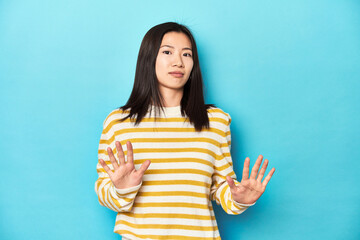 Wall Mural - Asian woman in striped yellow sweater, rejecting someone showing a gesture of disgust.