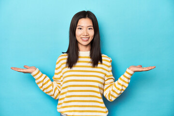 Wall Mural - Asian woman in striped yellow sweater, makes scale with arms, feels happy and confident.