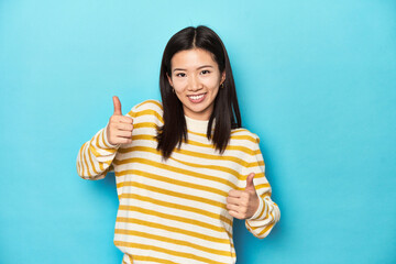 Wall Mural - Asian woman in striped yellow sweater, raising both thumbs up, smiling and confident.