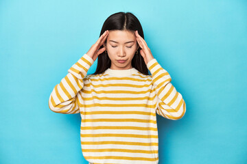 Wall Mural - Asian woman in striped yellow sweater, touching temples and having headache.