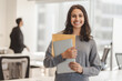© Maria Vitkovska - Smiling confident Indian woman wearing casual clothes holding laptop and documents, looking at camera at modern office. Good looking businesswoman posing for picture. Concept of successful business