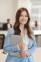 Portrait Of Positive Smiling Woman Holding Laptop While Standing In Modern Office. Attractive Confident Businesswoman Posing For Picture, Successful Career Concept