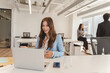 © Maria Vitkovska - Smiling american woman using laptop, having video call while sitting in modern office