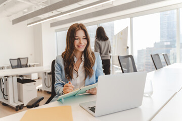 Wall Mural - Smiling american woman using laptop, having video call while sitting in modern office