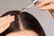 © New Africa - Woman applying essential oil onto hair roots on light grey background, closeup