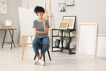 Poster - Young woman with brush palette near easel in studio