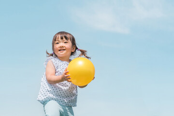 夏休みに青空の下でボール遊びをするアジア人の子供（女の子）