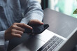 © tippapatt - Closeup of woman finger touching on mobile phone screen. Asian woman using smartphone while sitting at table with laptop computer at home office, online shopping, mobile banking, internet payment