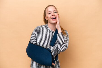 Canvas Print - Young caucasian girl with broken arm and wearing a sling isolated on beige background shouting with mouth wide open