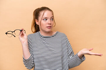 Wall Mural - Young caucasian girl with glasses isolated on beige background with surprise facial expression