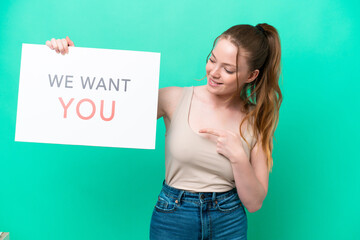 Canvas Print - Young caucasian woman isolated on green background holding We Want You board and  pointing it