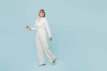 Wall Mural - Full body side view employee business woman 50s wears white classic suit glasses formal clothes walking going look aisde on area isolated on plain pastel blue background. Achievement career concept.