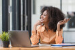 © Songsak C - Portrait of a beautiful confident businesswoman using a laptop computer holding a mobile phone sitting in a modern office. Smiling African American freelancer working online from home.