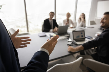 Wall Mural - Presenter speaking team of colleagues, office employees sitting at meeting table, looking at presenter. Male business leader giving presentation. Close up of hands with audience in blurred background