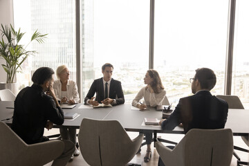 Wall Mural - Serious handsome young team leader man talking to colleagues on office meeting, explaining plan, strategy. Business partners discussing deal on conference room, negotiating on partnership