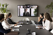 © fizkes - Business team and leader meeting online and offline, sitting at conference table, looking at interactive board with headshots, listening to speaker, CEO, discussing project on group video call